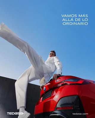 Hombre vestido de blanco saltando sobre la parte trasera de un auto deportivo rojo bajo cielo azul