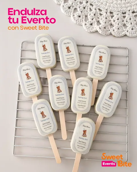Paletas blancas con etiqueta impresa de baby shower sobre rejilla metálica y tapete de crochet