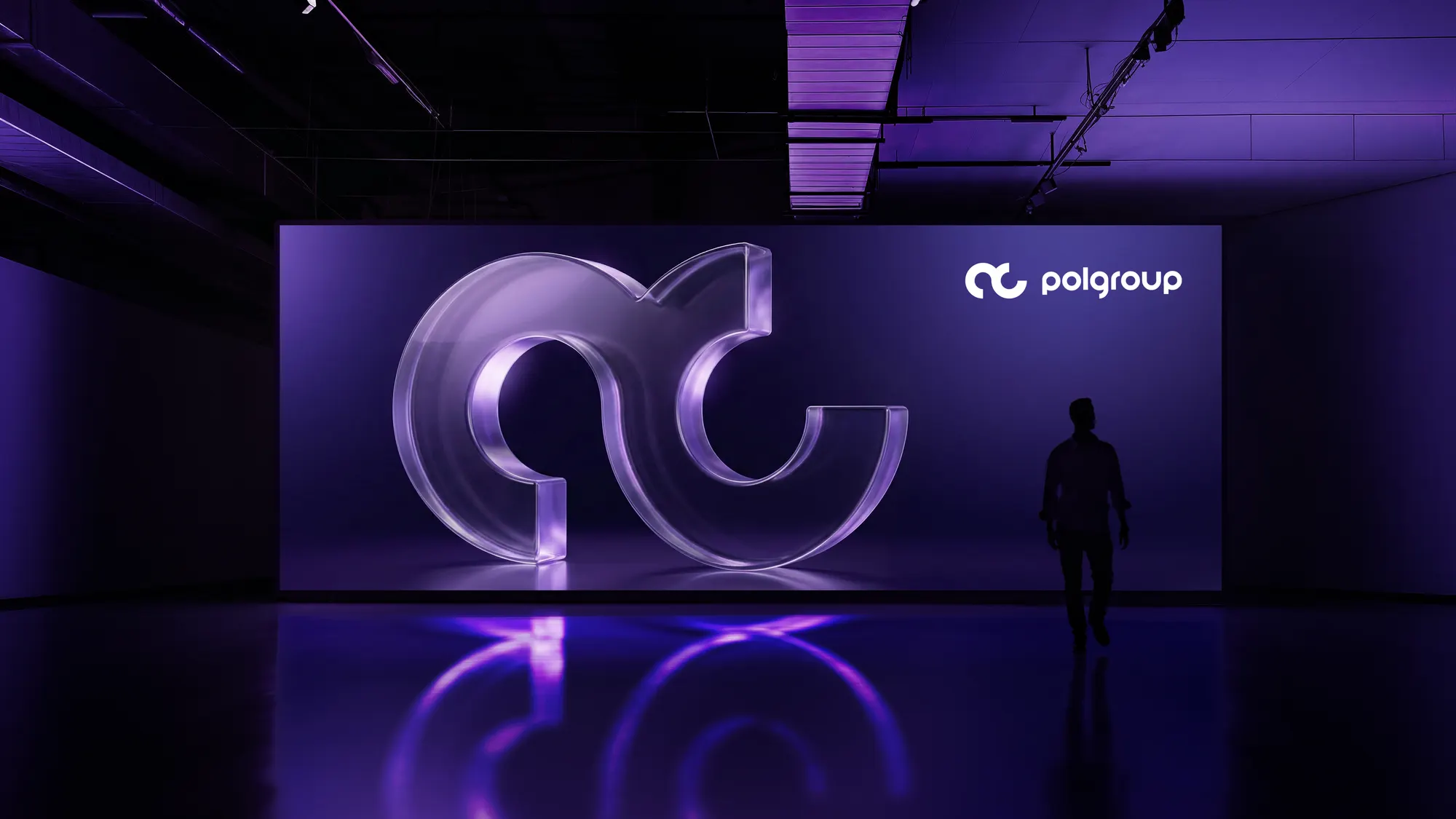 Instalación del isotipo iluminado de Polgroup en un espacio oscuro, con la silueta de una persona caminando